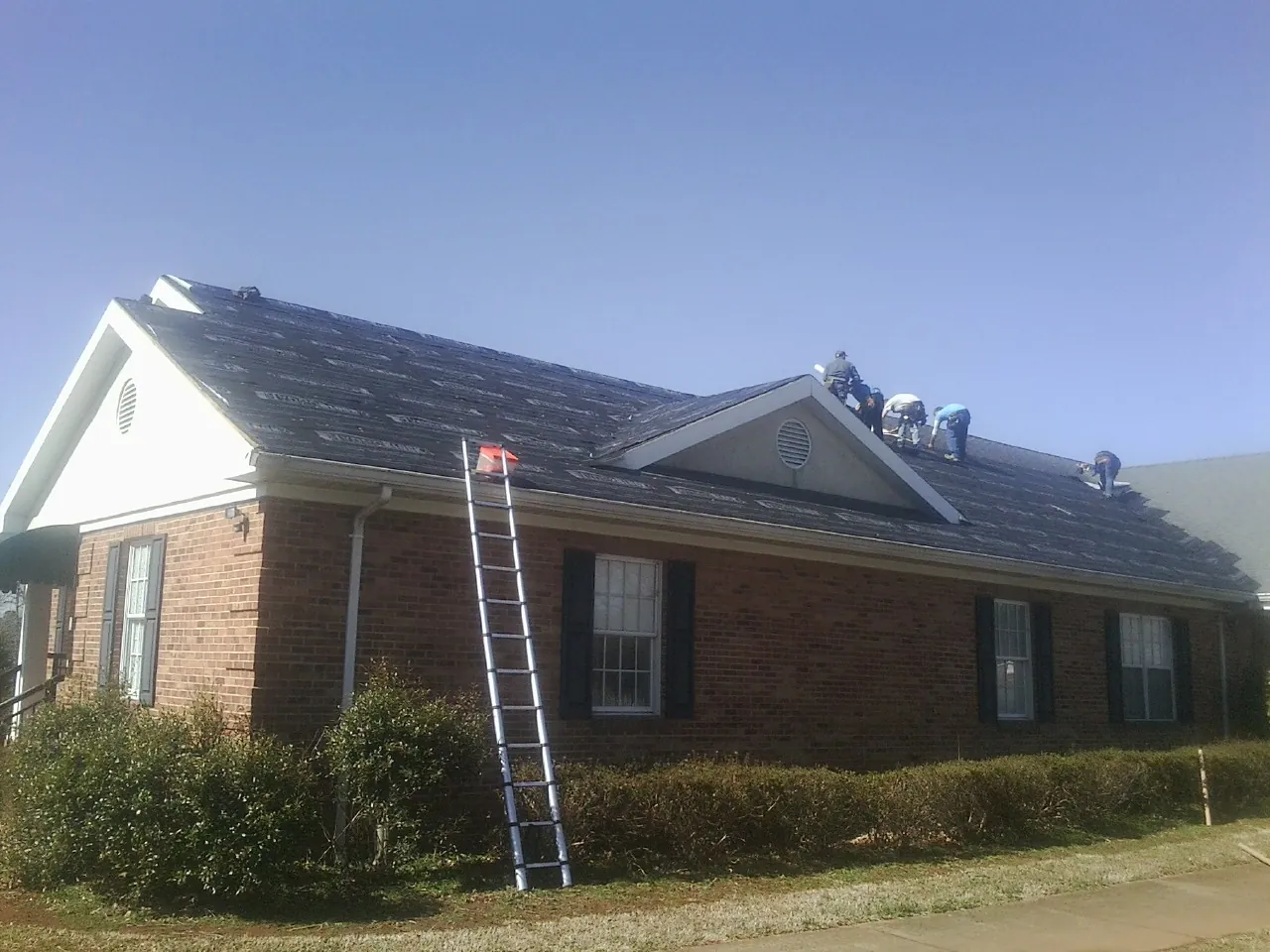 Crew tearing shingles off a brick ranch roof with a ladder set — Emergency Roof Repair work by our crew in Winona Lake