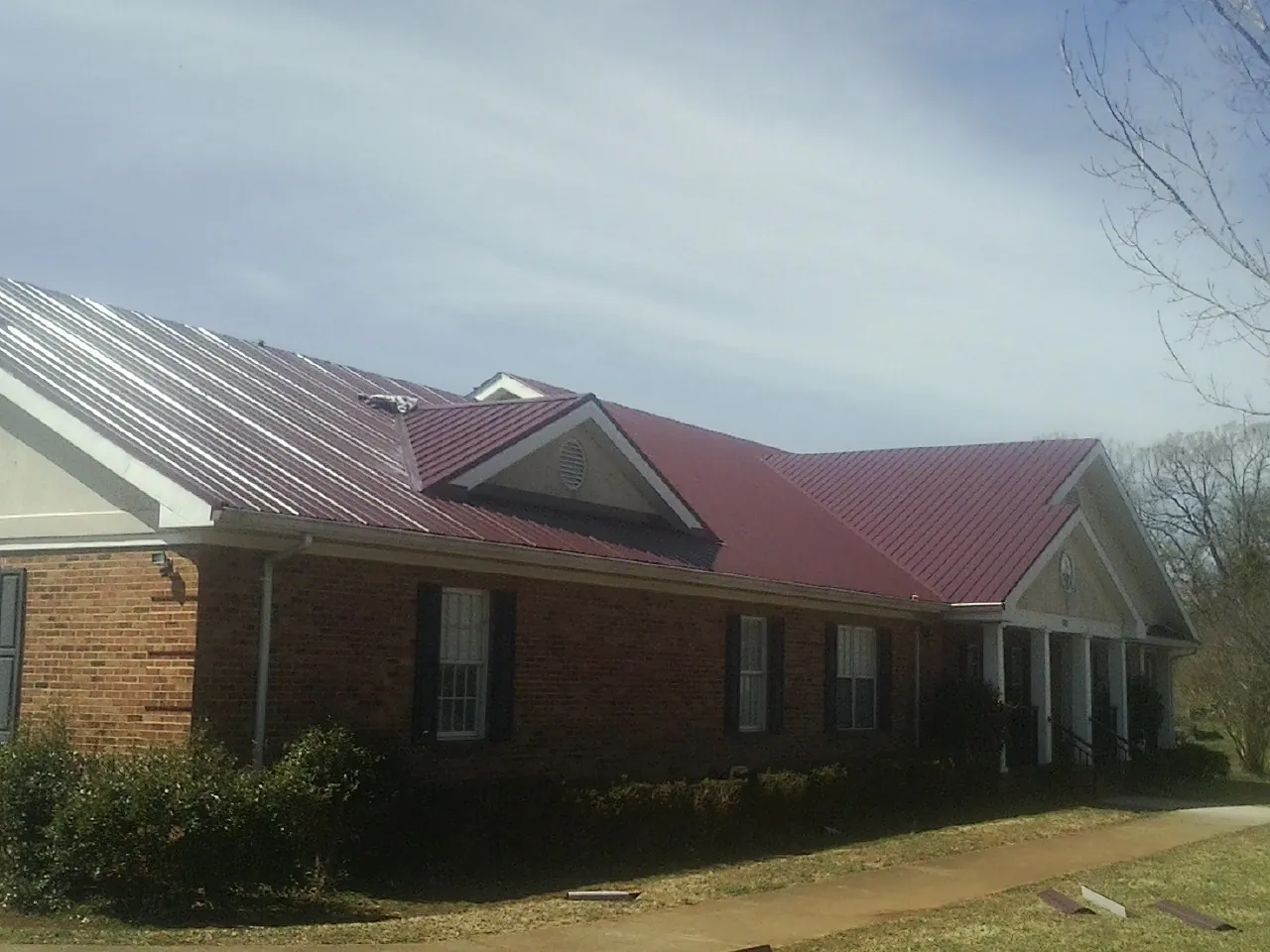 Red metal roof with gabled entries on a long brick building, from a Hail Damage Roof Repair job in Winona Lake