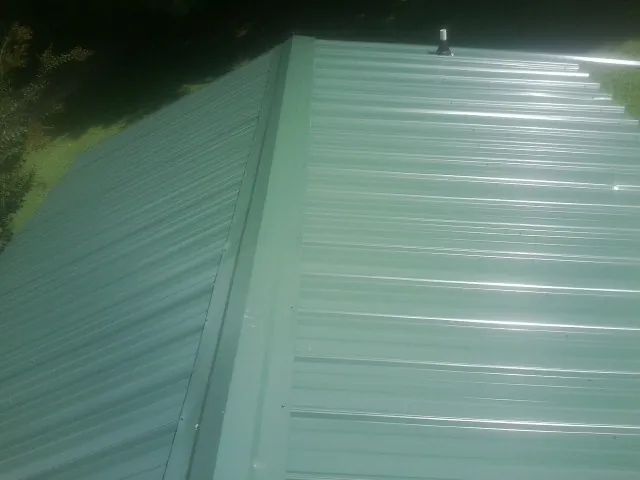 New green metal panels meeting at the ridge of a roof — Flat Roof Repair work by our crew in Winona Lake
