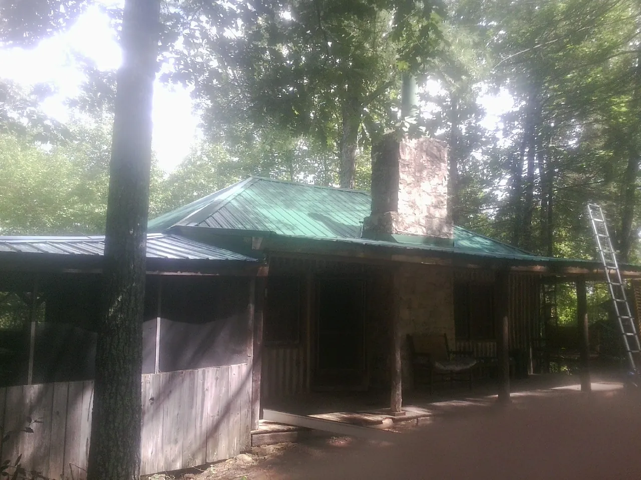 Green metal roof and stone chimney above a log cabin porch in Winona Lake