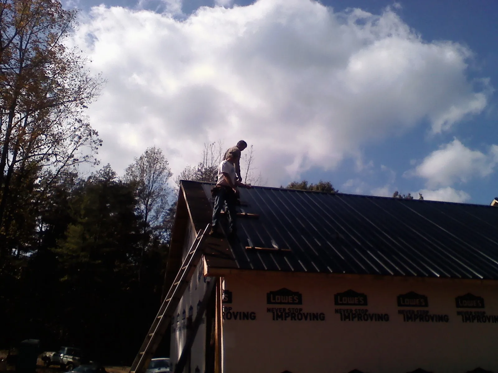 Roofer fastening dark metal panels high against a cloudy sky, from a Roof Inspection job in Winona Lake