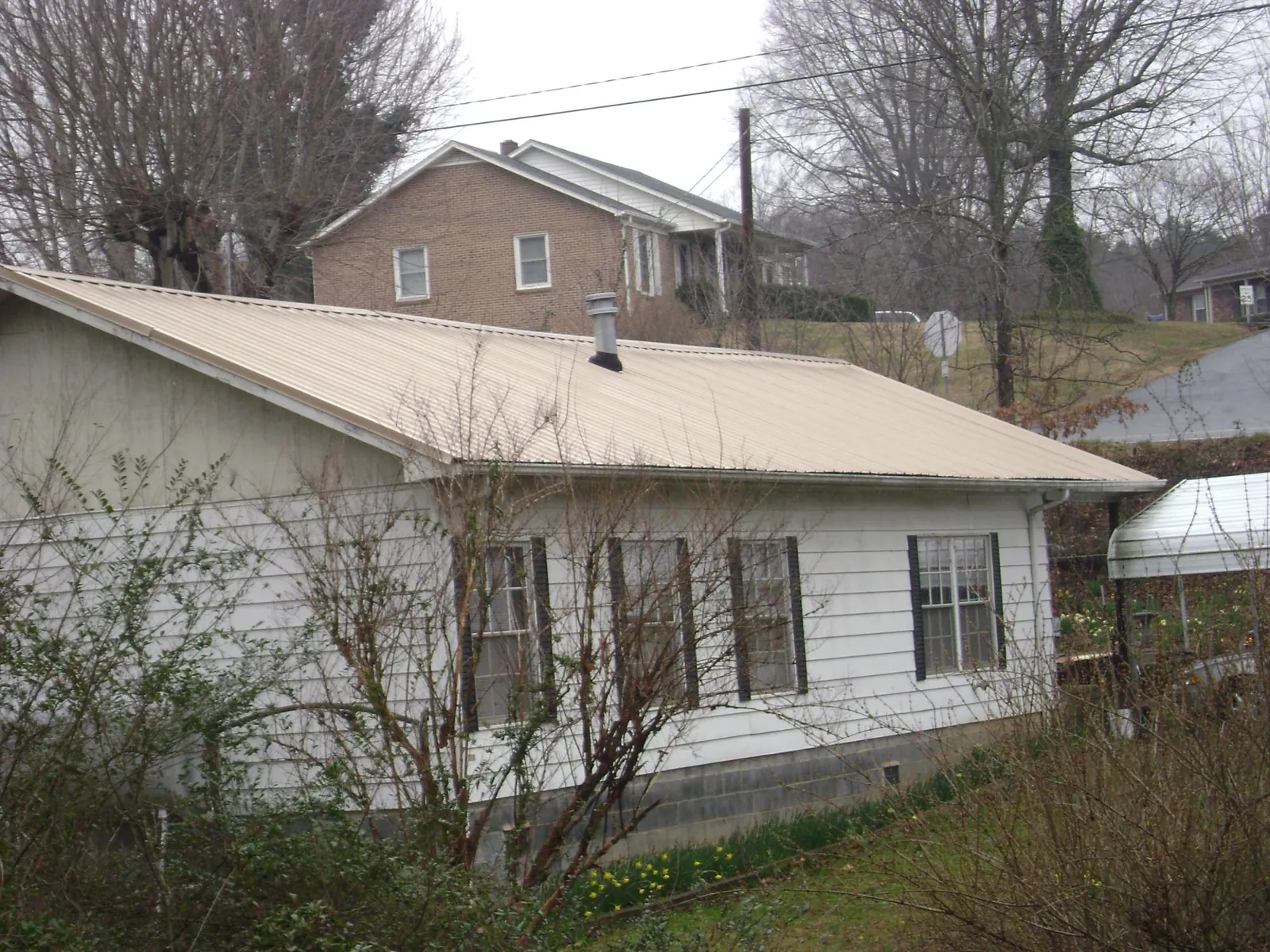 Tan metal roof on a white sided house set into a hillside — Commercial Roofing by Roofing Brothers in Winona Lake