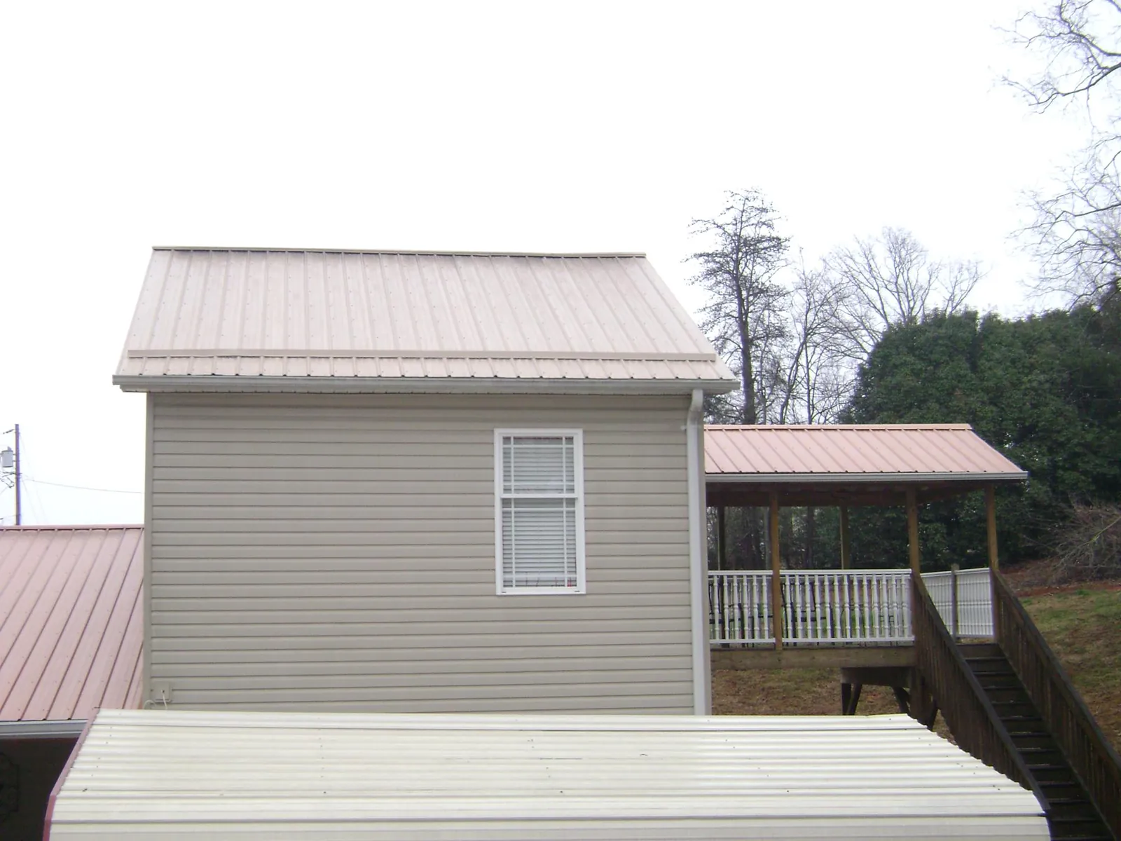 Tan metal roofs on a two story addition and attached porch, from a Roof Replacement job in Winona Lake